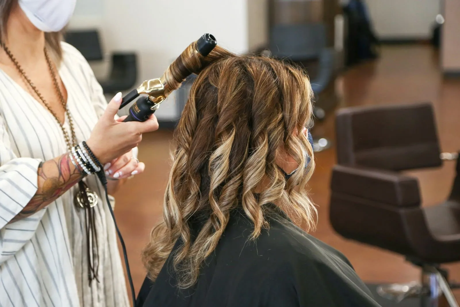 Frisør krøller en kundes halvlange, lysnede hår med et krøllejern i en salon