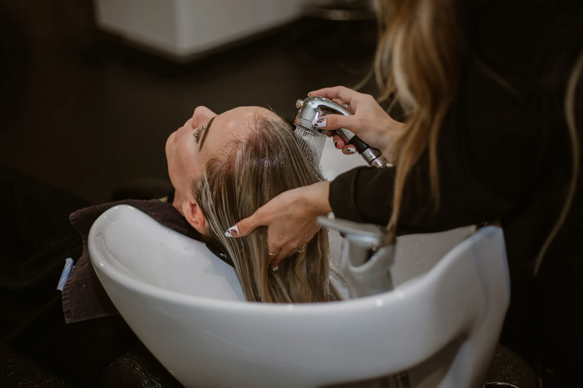 Frisør skyller langt, lyst hår på en kunde ved en hårvask i en salon